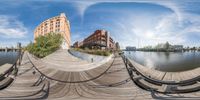 a fish eye photo of a boardwalk in a city by the water, with buildings behind it