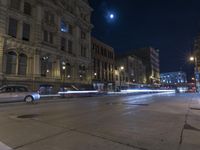 a night time view of city streets with buildings and a car driving at the same lane