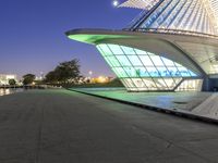 the building is lit up in bright green lights at night, near a waterway and walkway
