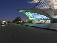 the building is lit up in bright green lights at night, near a waterway and walkway