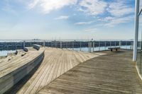 a dock is lined with benches along the water near a beach on a partly sunny day