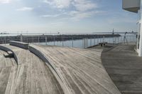 a dock is lined with benches along the water near a beach on a partly sunny day