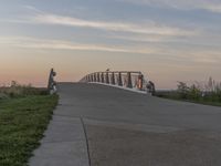 a couple of people sitting on the bench near the end of a walkway while the sun is rising