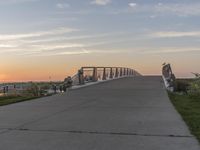 a couple of people sitting on the bench near the end of a walkway while the sun is rising