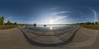 a panorama fish eye view shows two boats at a marina bay and the sun setting