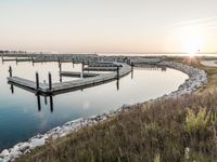 a marina is on the shore of a lake with a pier and sun in the background