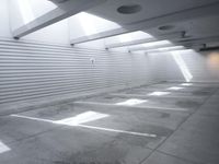 the white wall of an empty parking garage has holes in the concrete and sunlight streaming through