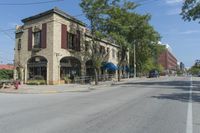 an empty street surrounded by tall buildings and trees in a town with people riding motorcycles