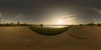 a fish - eye view of the sun over a body of water and buildings in the distance