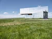 the large mirror building is reflecting into the green field of grass and tall grasses below the mirrored glass building