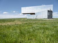 the large mirror building is reflecting into the green field of grass and tall grasses below the mirrored glass building