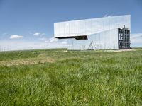 the large mirror building is reflecting into the green field of grass and tall grasses below the mirrored glass building