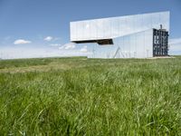 the large mirror building is reflecting into the green field of grass and tall grasses below the mirrored glass building