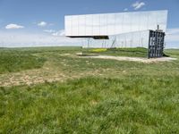 the large mirror building is reflecting into the green field of grass and tall grasses below the mirrored glass building