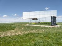 the large mirror building is reflecting into the green field of grass and tall grasses below the mirrored glass building