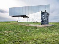 a large mirror sits in the middle of grass outside a building with a sky background