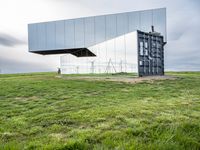 a large mirror sits in the middle of grass outside a building with a sky background