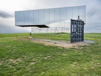 a large mirror sits in the middle of grass outside a building with a sky background