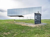 a large mirror sits in the middle of grass outside a building with a sky background