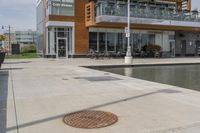 a manhole in the sidewalk beside water features many small potted plants and chairs