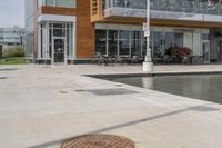 a manhole in the sidewalk beside water features many small potted plants and chairs