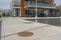 a manhole in the sidewalk beside water features many small potted plants and chairs