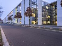 an empty street with a big white building in the background at dusk, on the side