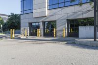 there is a large parking lot on the sidewalk by the building with yellow poles in front