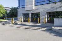 there is a large parking lot on the sidewalk by the building with yellow poles in front