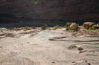 two people standing on rocks looking at something in the distance, along a canyon side path