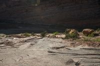 two people standing on rocks looking at something in the distance, along a canyon side path