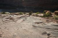 two people standing on rocks looking at something in the distance, along a canyon side path