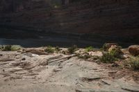 two people standing on rocks looking at something in the distance, along a canyon side path