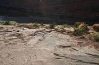 two people standing on rocks looking at something in the distance, along a canyon side path