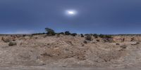 a wide angle picture shows the sun on top of a mountain in the desert beneath a blue sky