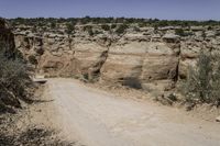 a road in the desert with large rocky sides and greenery on both sides of it