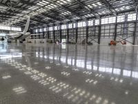 an airplane in an indoor hangar filled with windows, reflections, and concrete flooring