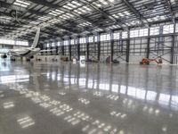 an airplane in an indoor hangar filled with windows, reflections, and concrete flooring