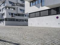 a brick driveway is next to a modern apartment building with two floors, with several windows