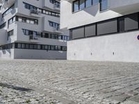 a brick driveway is next to a modern apartment building with two floors, with several windows