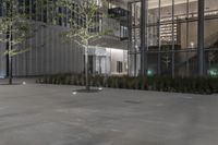 a concrete sidewalk in front of a building with some windows at night time near by