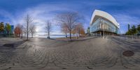 a circular panorama fisheye of a building near the water on a street corner with many trees