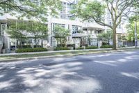 a road leading to some apartment buildings with cars on the curb and trees along it