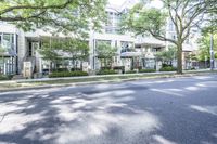 a road leading to some apartment buildings with cars on the curb and trees along it