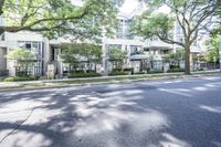 a road leading to some apartment buildings with cars on the curb and trees along it