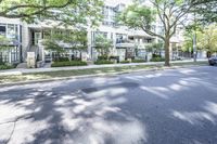 a road leading to some apartment buildings with cars on the curb and trees along it