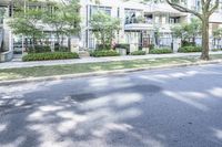 a road leading to some apartment buildings with cars on the curb and trees along it