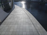 a large cement building next to water with sun shining in it's reflection on the glass wall