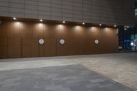 a wall with five circular light fixtures, all on a tile surface, in front of a brown building