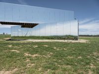 a large mirror is sitting in a grassy field by some rocks and the sky with white clouds